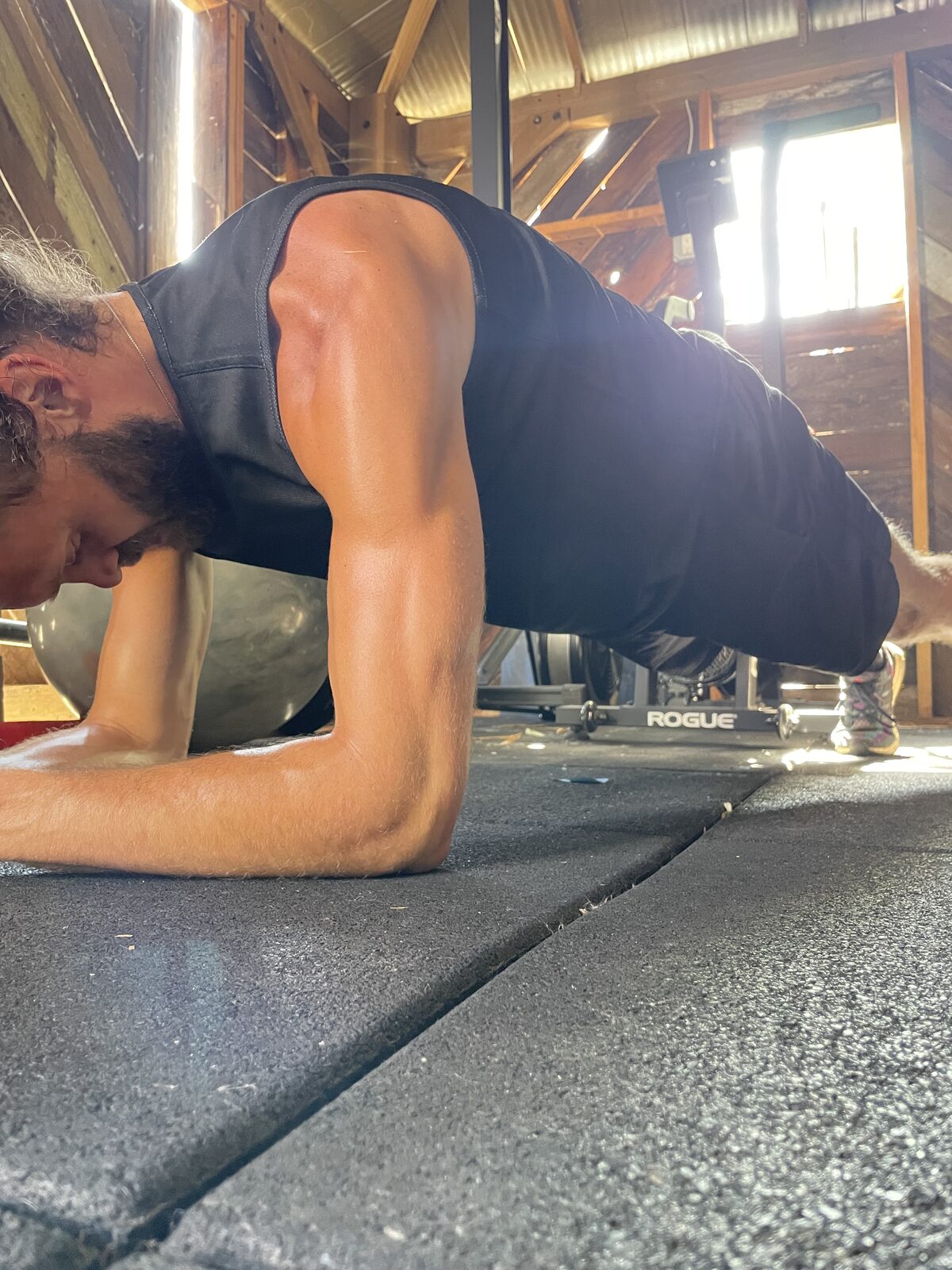 A person holding a forearm plank in the wood-beam training barn