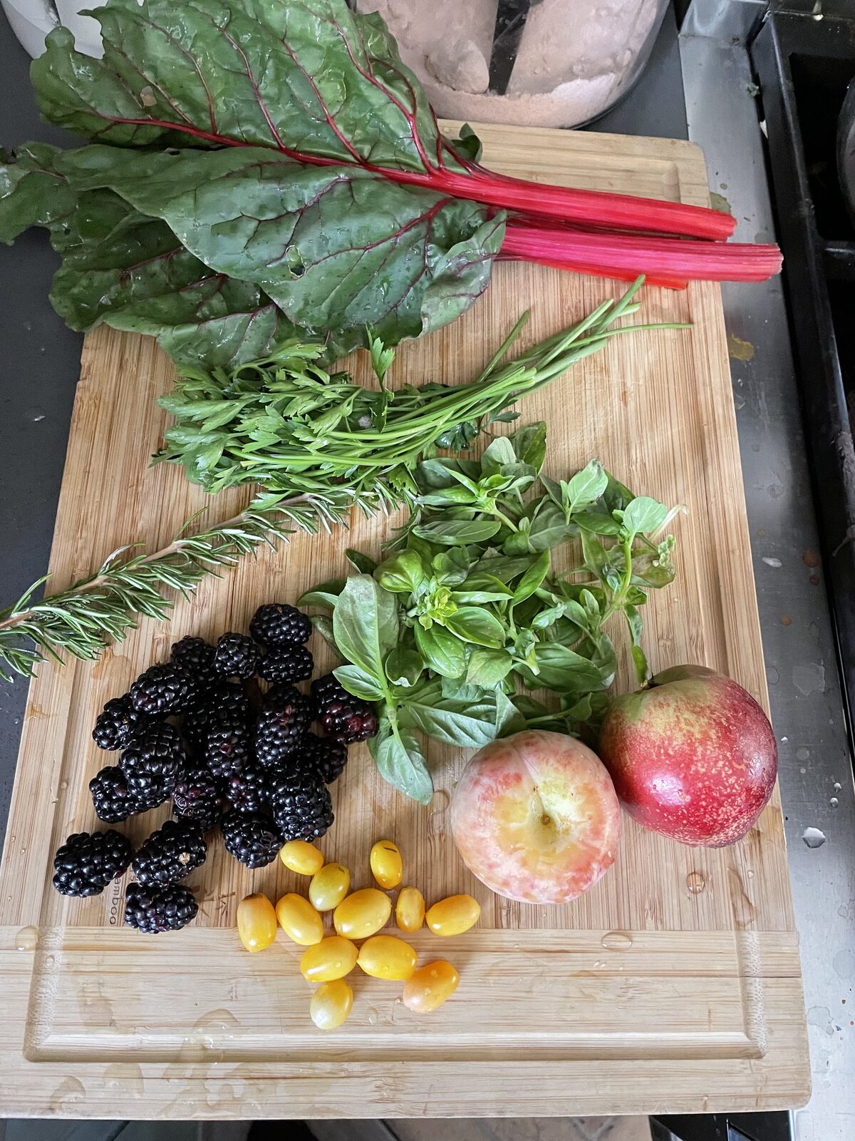 A cutting board with freshly harvested chard, herbs, apples and cherry tomatoes